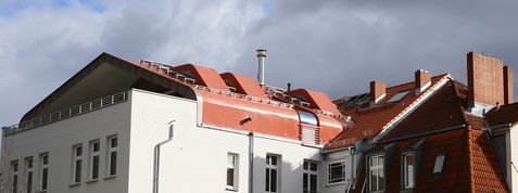 Dach mit roten Ziegeln und weißer Fassade eines mehrstöckigen Gebäudes unter blauem Himmel