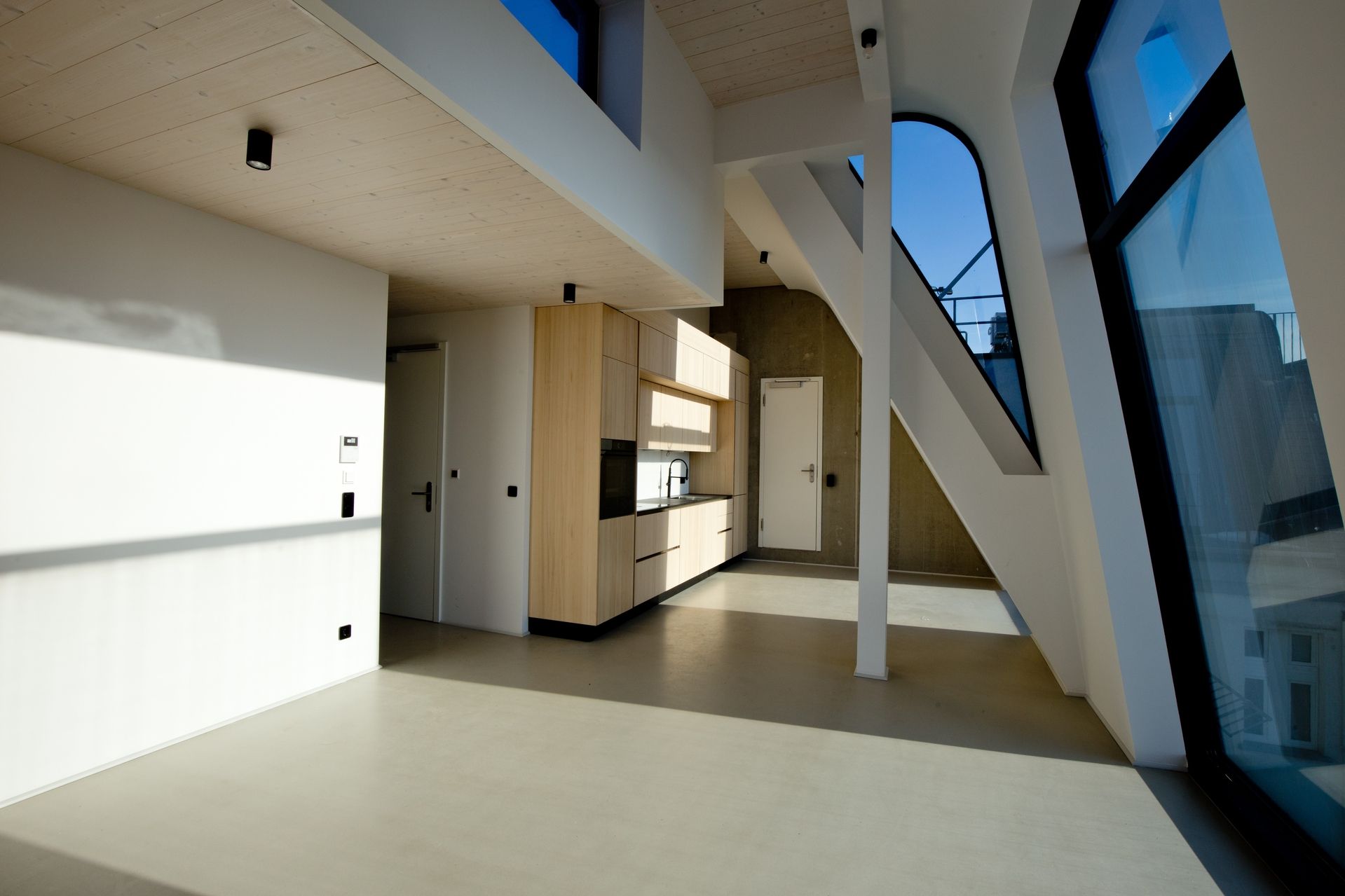 Helle moderne Wohnung mit offener Küche, großen schrägen Fenstern und sichtbaren Stahlträgern