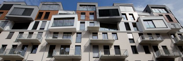 Fassade eines modernen Wohngebäudes mit mehreren Balkonen und großen Fenstern unter blauem Himmel