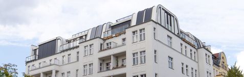 Mehrstöckiges Wohngebäude mit weißen Fassaden und mehreren Balkonen unter bewölktem Himmel