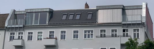 Oberer Teil eines mehrstöckigen Gebäudes mit mehreren Fenstern, Dachfenstern und Balkonen