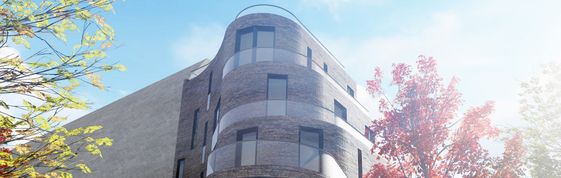 Gebäude mit abgerundeter Fassade und mehreren Fenstern vor blauem Himmel und Bäumen mit grünen und roten Blättern