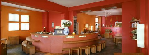 Innenraum eines Restaurants mit orangefarbenen Wänden, einer runden Theke und mehreren Holzhockern