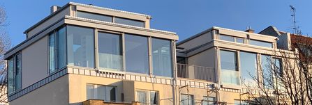 Dachterrassen mit großen Glasfenstern und Geländern an einem modernen Wohngebäude bei klarem Himmel
