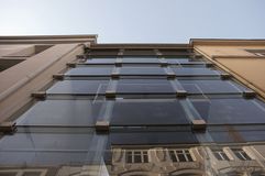 Blick von unten auf einen modernen Glastrakt zwischen zwei historischen Gebäuden mit sichtbarer Fassade im unteren Bereich