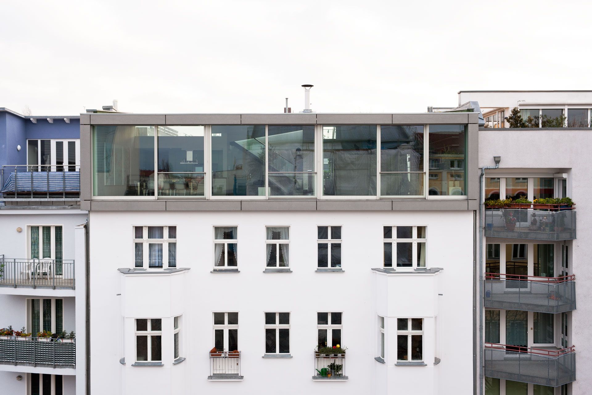 Moderner verglaster Dachaufbau auf einem klassischen weißen Wohngebäude mit mehreren Fenstern und Balkonen